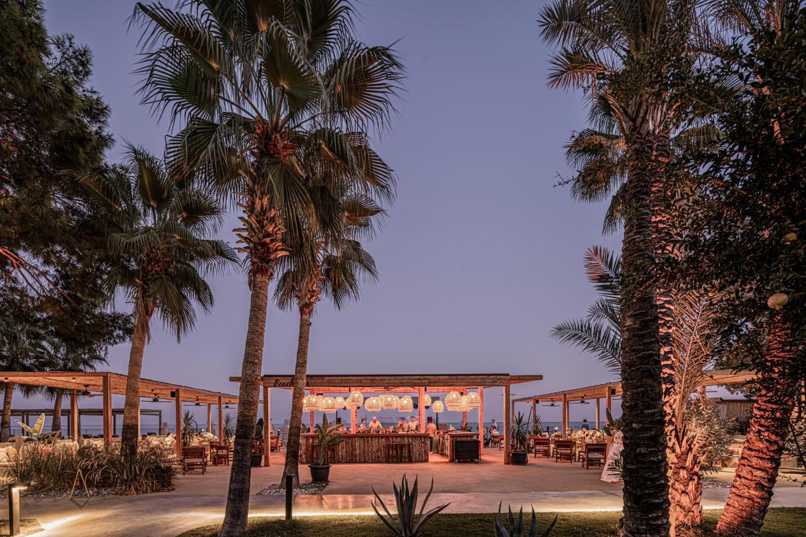 Balmy Beach Resort Kemer pludmales bārs vakarā ar izgaismotām palmām un dekoratīvām lampām piekrastē