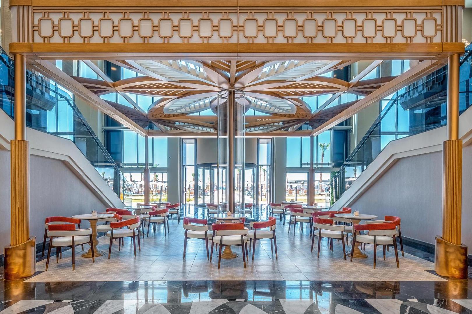 Lago Hotel gaišā atpūtas zona ar dizaina griestiem zieda formā, moderniem krēsliem un skatu uz āra teritoriju
