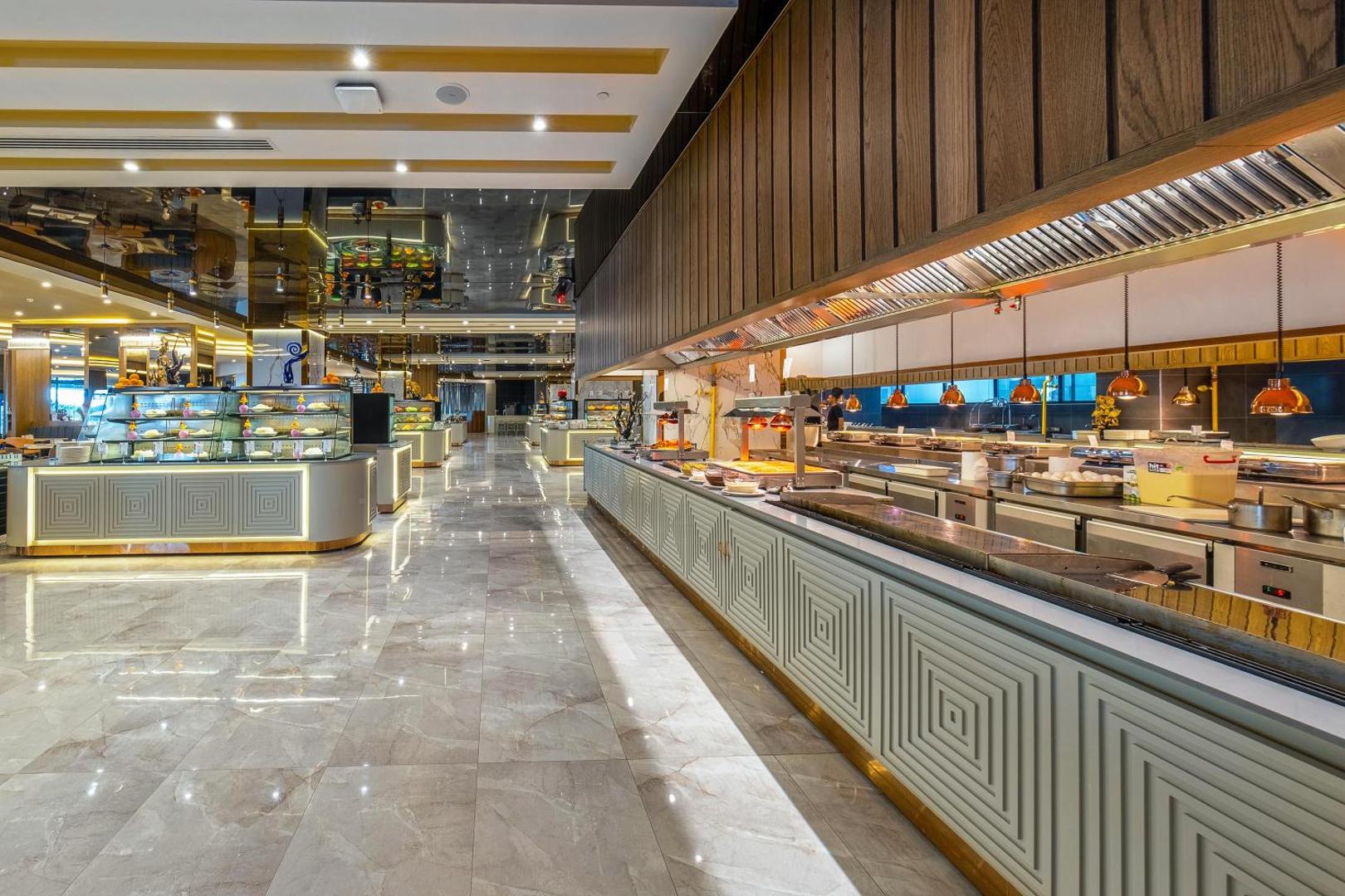 Lago Hotel galvenā restorāna bufetes zona ar plašu ēdienu izvēli, modernu apgaismojumu un spīdīgām marmora grīdām Antaljas reģionā