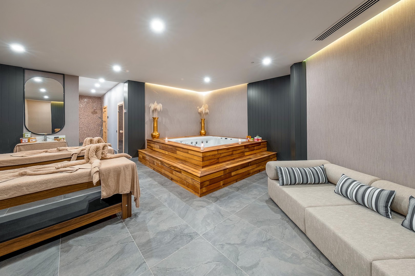 Lago Hotel spa centrs ar masāžas galdiem un koka apdares džakuzi — mājīga relaksācijas telpa mierīgai atpūtai