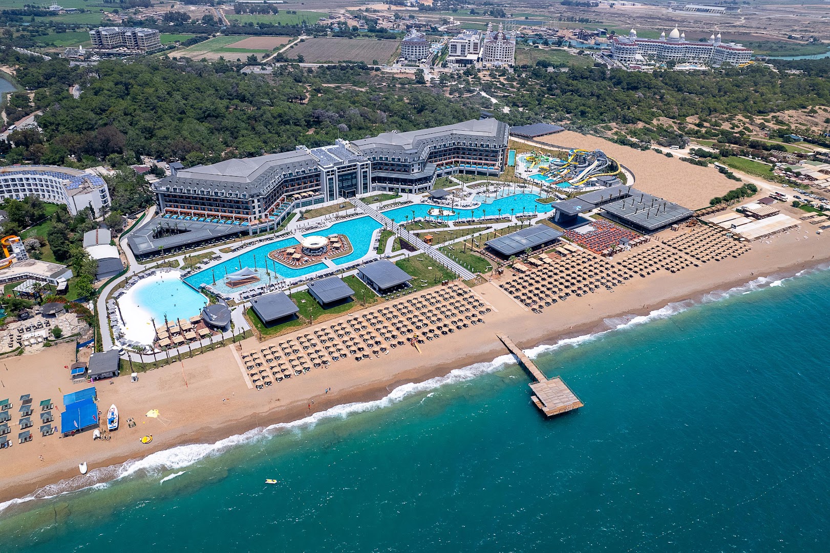 Lago Hotel aerofoto ar akcentu uz baseinu kompleksu un akvaparku — tirkīza ūdens, bāri un atpūtas zonas pie pludmales