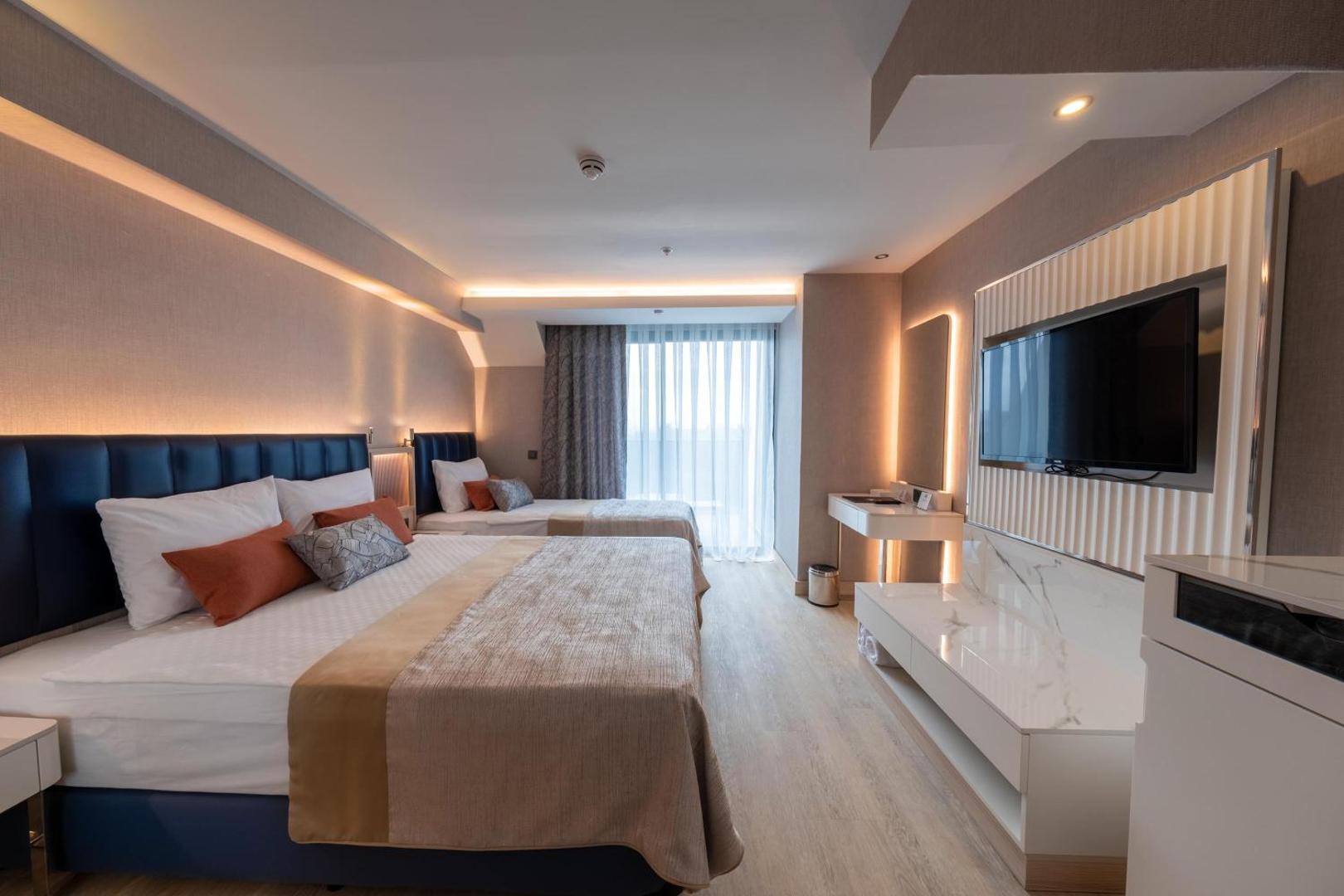 Lago Hotel plašs numurs ar divām gultām, sienas televizoru un modernu apgaismojumu siltos toņos piekrastes viesnīcā