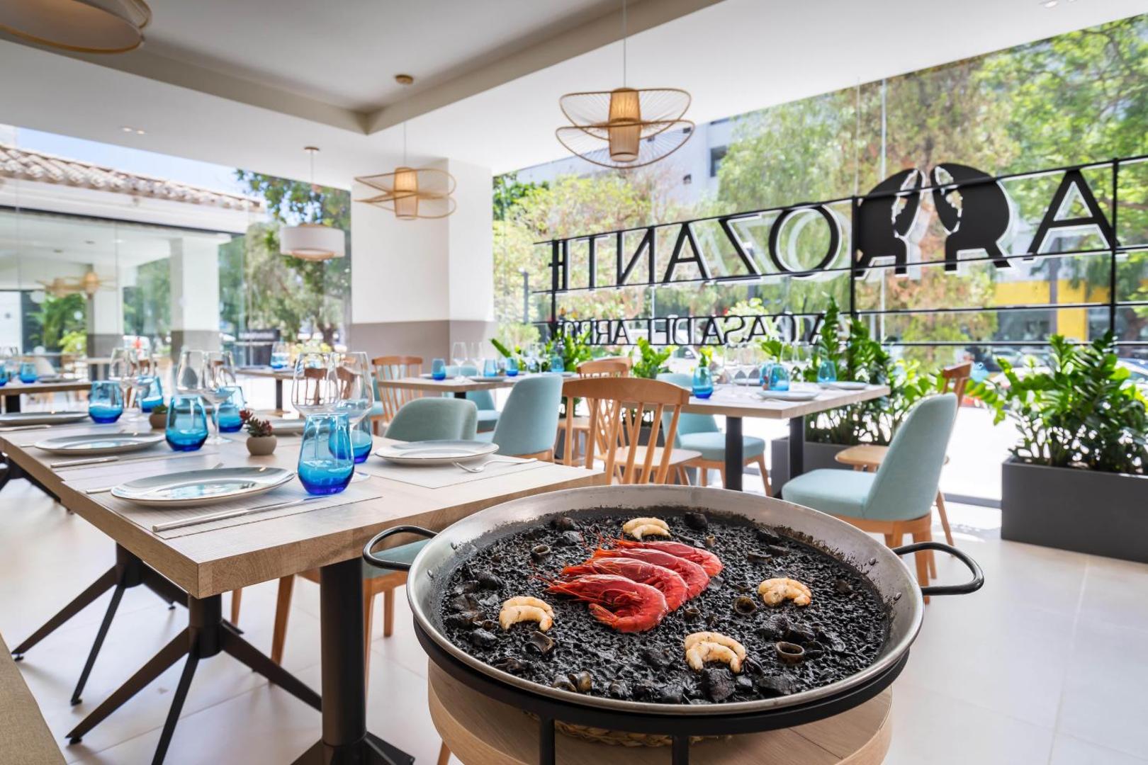 Occidental Puerto Banus restorāna interjers ar servētiem galdiem un melno paelju ar garnelēm priekšplānā