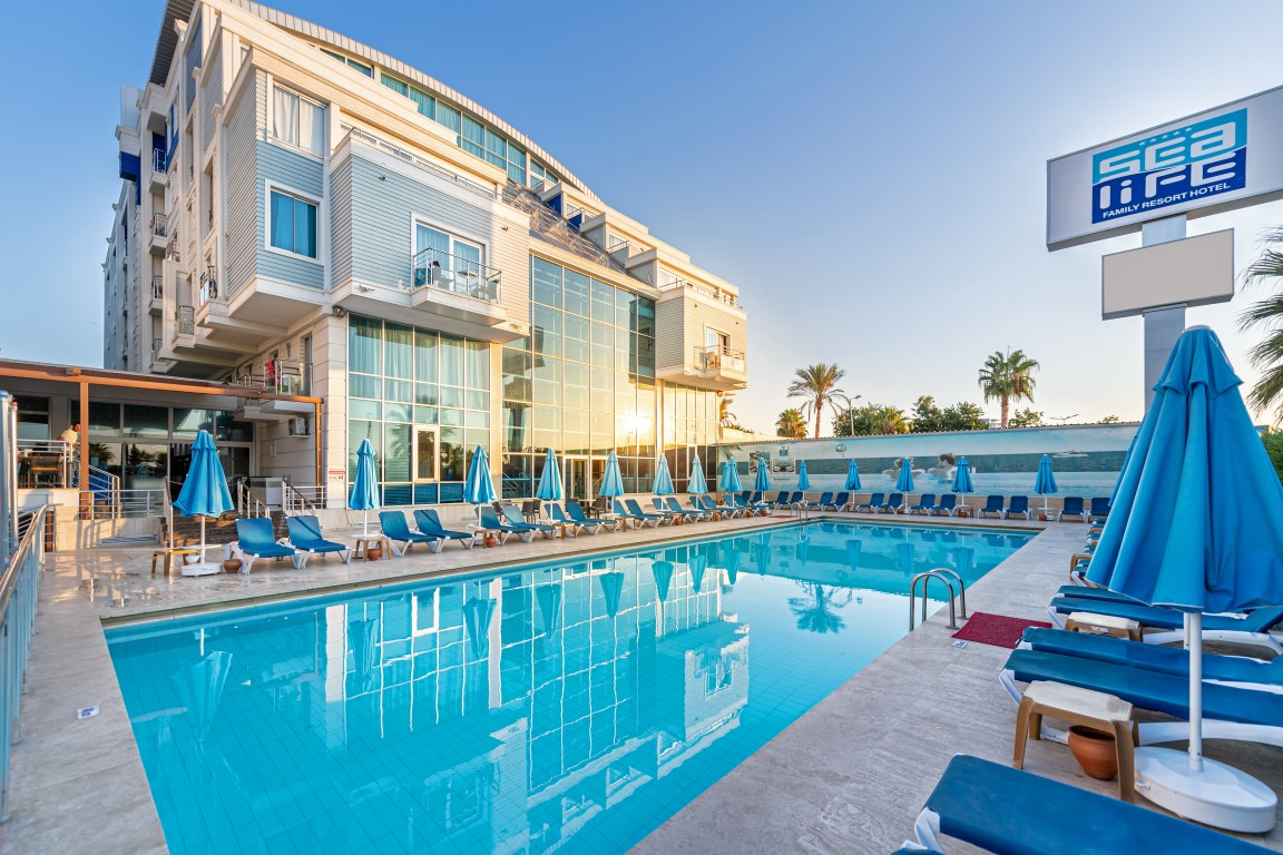 Sealife Family Resort Hotel āra baseins saulrietā Antaljā, Turcijā — atpūtas zona ar ziliem saulessargiem un guļamkrēsliem pie viesnīcas ēkas