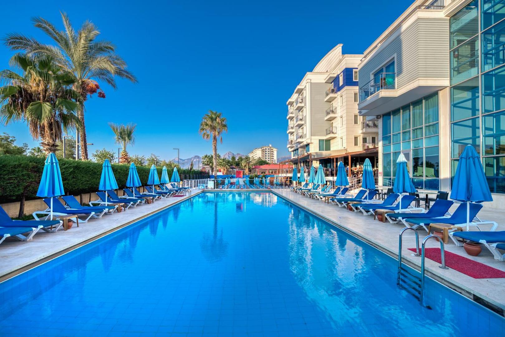 Sealife Family Resort Hotel āra baseins ar ziliem saulessargiem un zviļņiem pie viesnīcas ēkas Antaljā