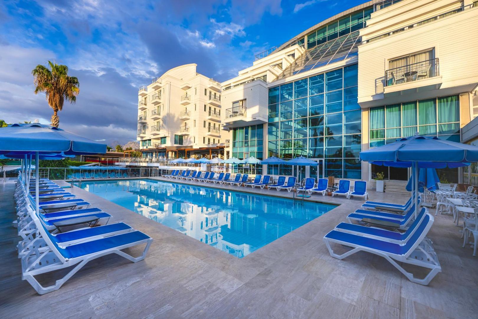 Sealife Family Resort Hotel modernā fasāde un plašais āra baseins vakarā — labiekārtota teritorija ar ērtiem zviļņiem un palmām