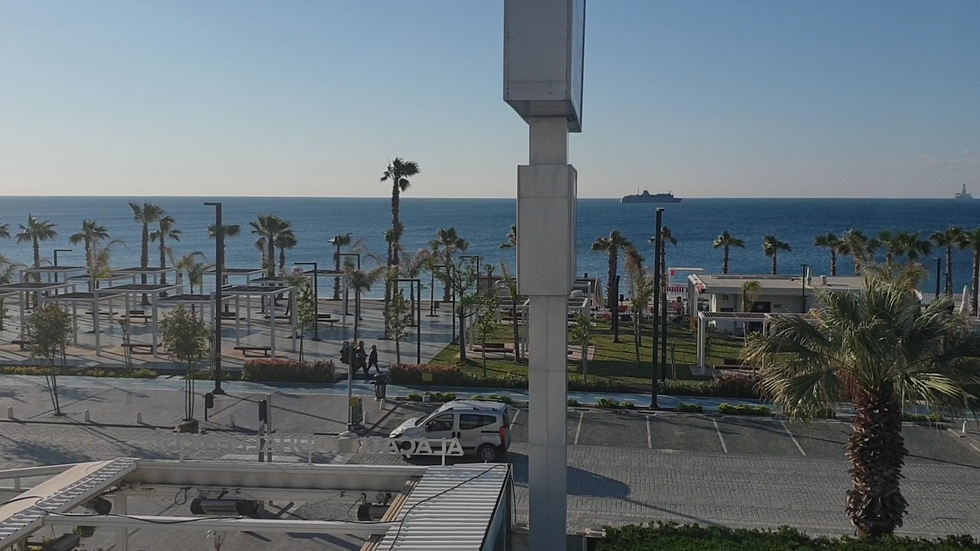 Skats no Sealife Family Resort Hotel uz Antālijas piekrastes promenādi, palmām un Vidusjūru ar kuģi tālumā saulainā dienā