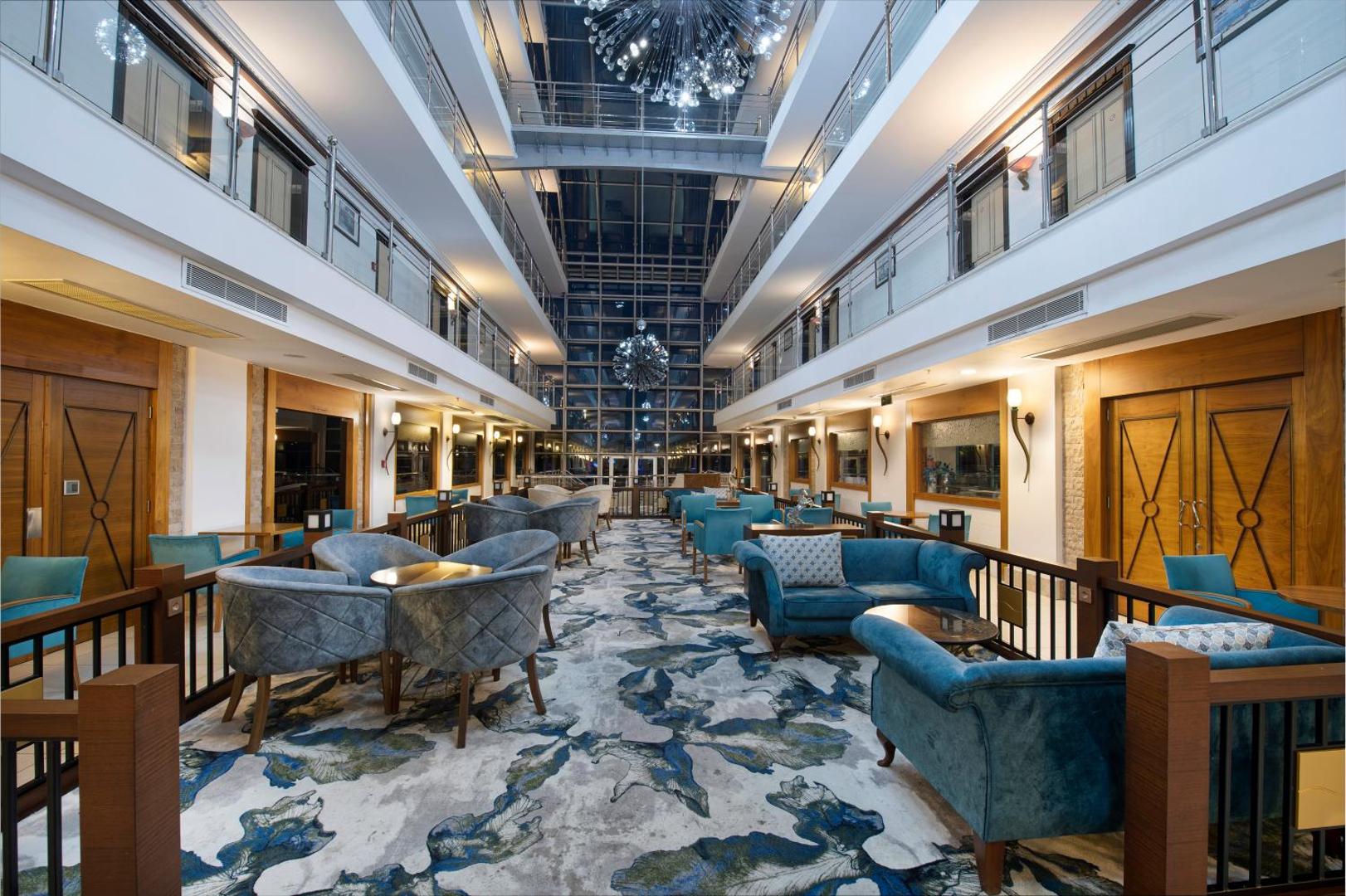 Sealife Family Resort Hotel atpūtas telpa ar ziliem dīvāniem, rakstainu paklāju un stikla jumta konstrukciju Antaljā