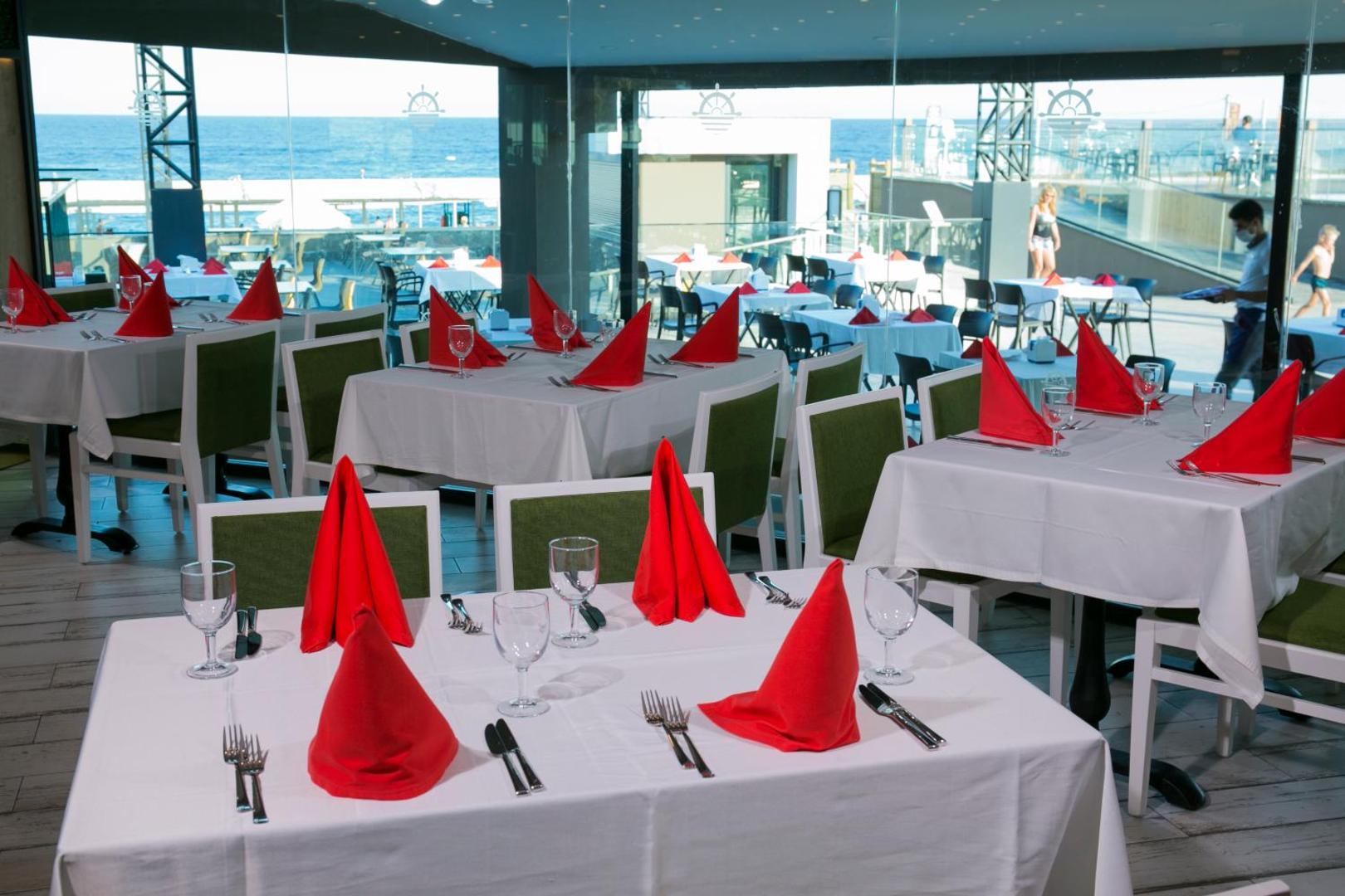 Sailor's Beach Club à la carte restorāna interjers ar eleganti klātiem galdiem un panorāmas logiem uz jūru