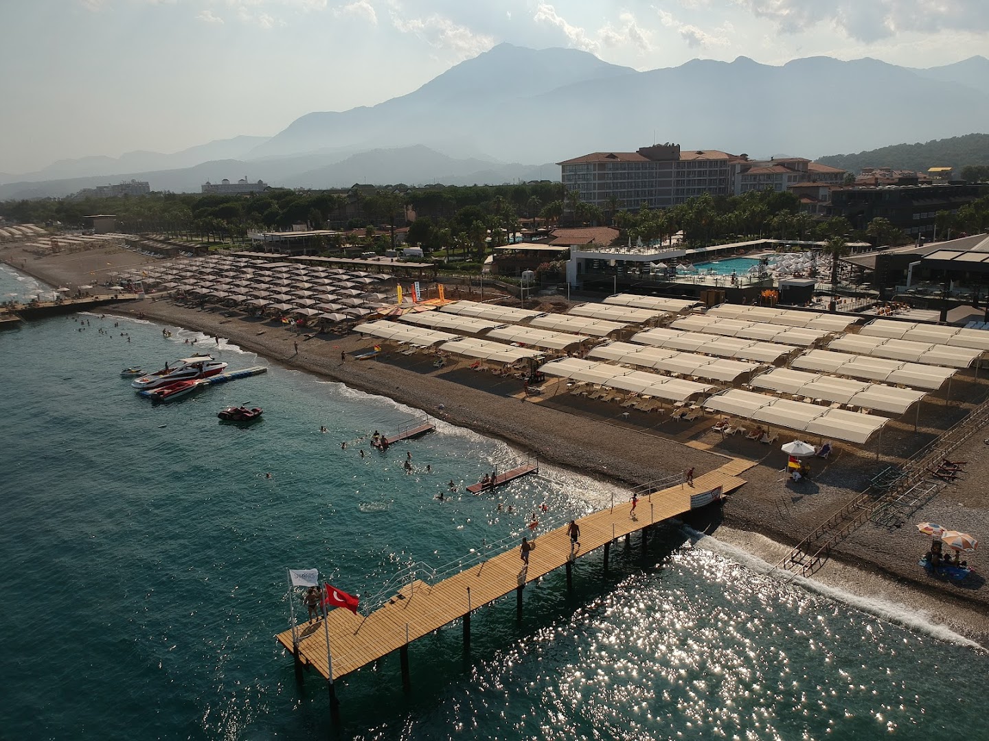Skats uz Sailor's Beach Club pludmali, koka piestātni un kalniem fonā saulainā dienā Kemeras reģionā