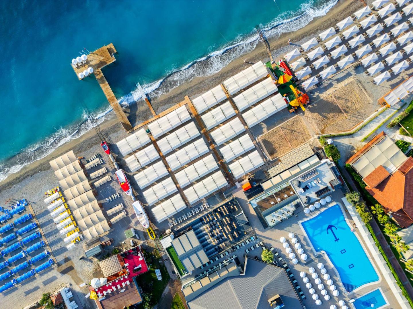 Sailor's Beach Club aerofoto skats uz pludmali, zilo baseinu ar enkura simbolu un saulessargu zonām Kemeras piekrastē