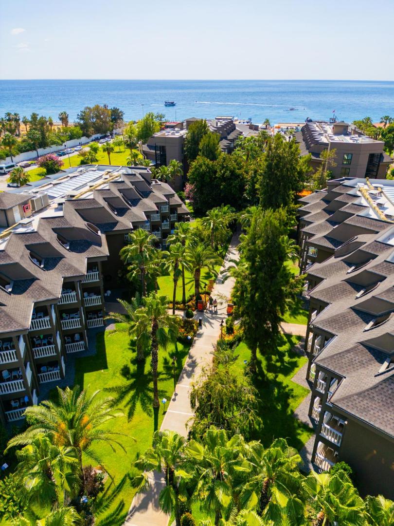 Sailor's Beach Club viesnīcas korpusi ar balkoniem, ko ieskauj kupls palmu dārzs un skats uz zilo jūru tālumā