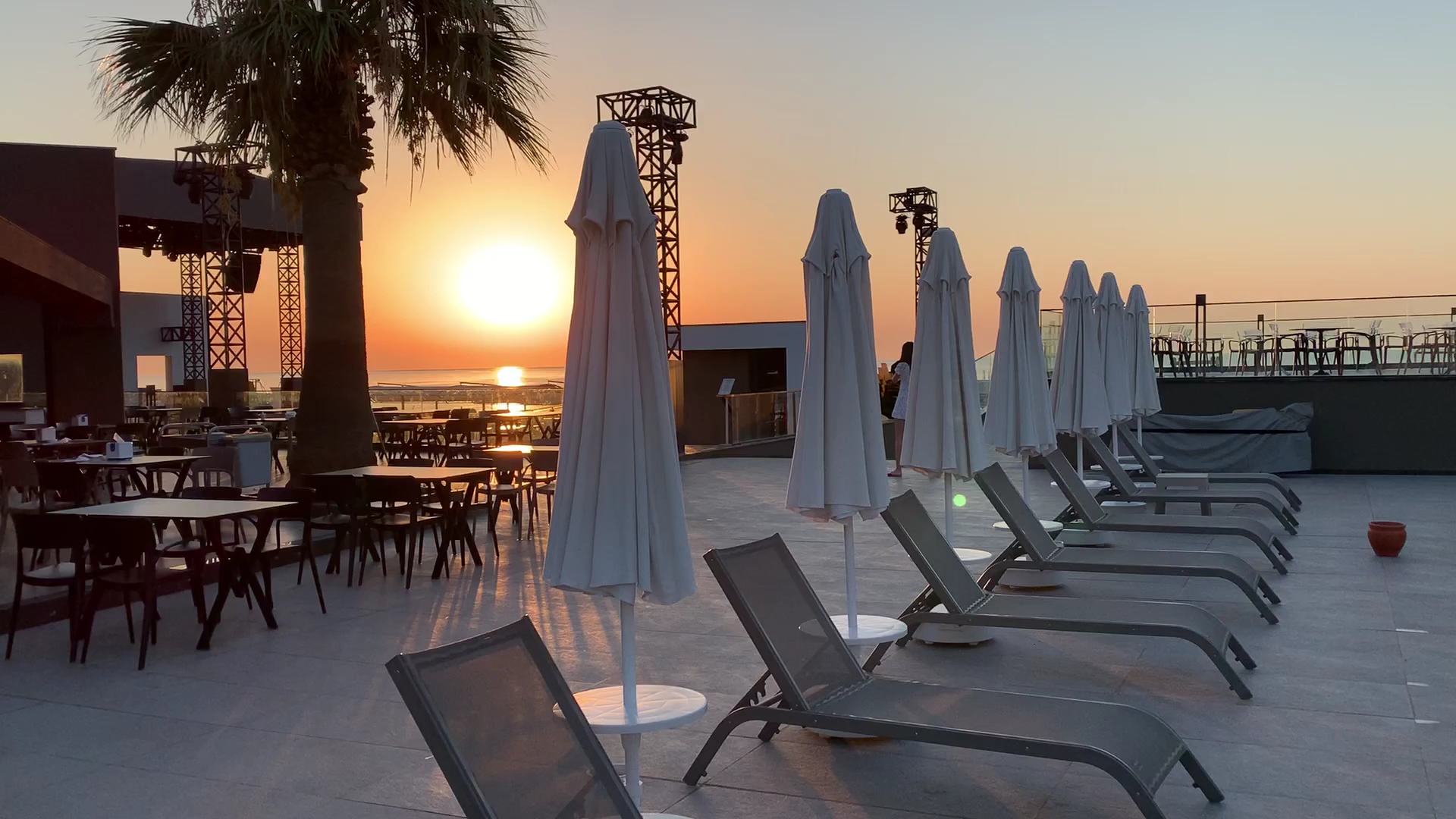 Saulriets Sailor's Beach Club terasē ar sauļošanās krēsliem un saulessargiem, skats uz jūru vakara gaismā