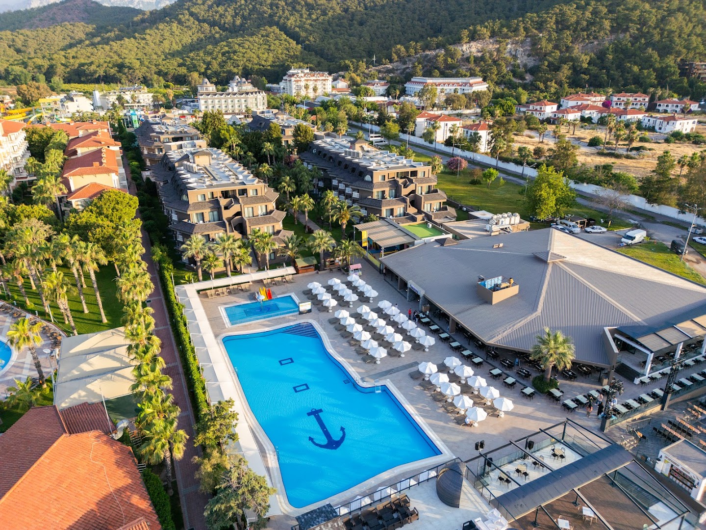 Sailor's Beach Club viesnīcas teritorijas skats no augšas ar galveno baseinu enkura formā, restorāna zonu un apkārtējiem zaļumiem Kemerā