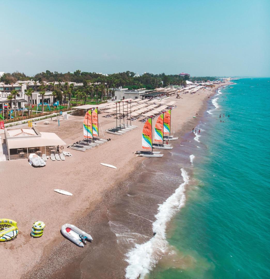 Paloma Orenda piekrastes panorāma ar ūdens sporta inventāru, katamarāniem un plašu smilšu pludmali Sides reģionā