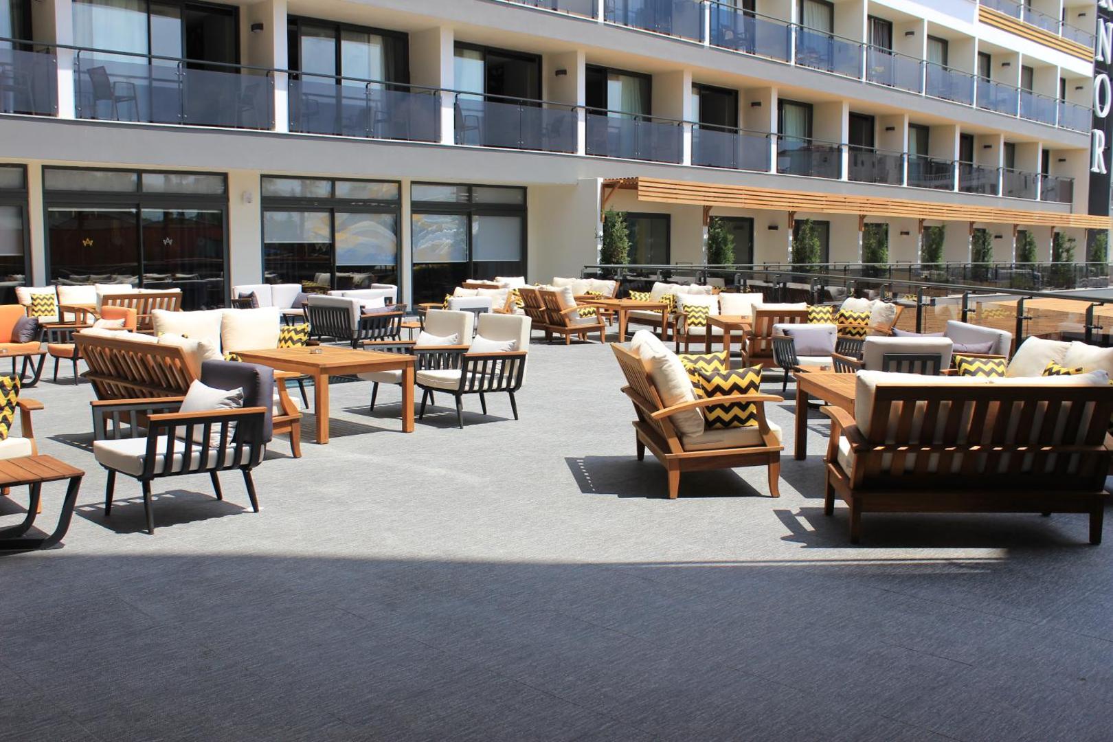 Arnor De Luxe Hotel & Spa plašā āra atpūtas terase ar mīkstajiem krēsliem, dīvāniem un koka galdiņiem pie viesnīcas fasādes.