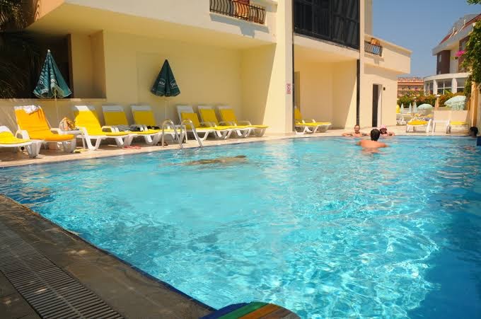 Camyuva Beach Hotel āra baseins ar peldētājiem un dzelteniem sauļošanās krēsliem pie viesnīcas ēkas Kemeras piekrastē