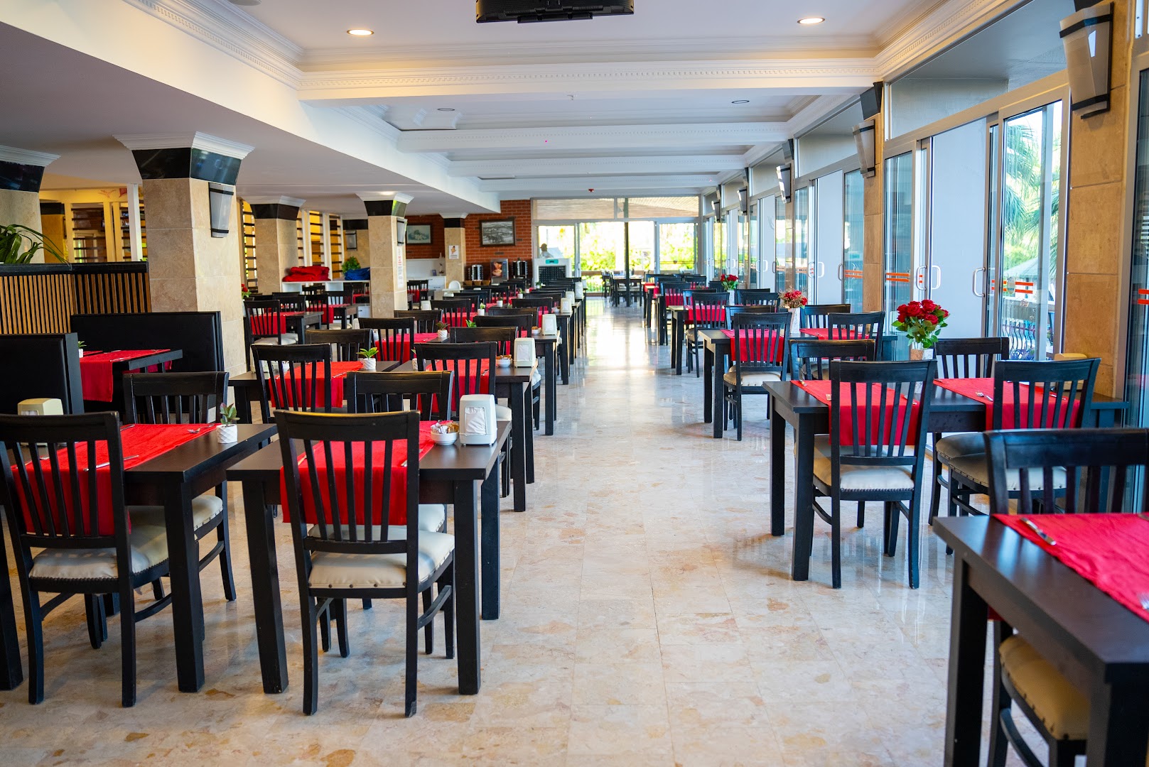 Camyuva Beach Hotel galvenā restorāna iekštelpas ar klātiem galdiem, sarkaniem akcentiem un lieliem panorāmas logiem