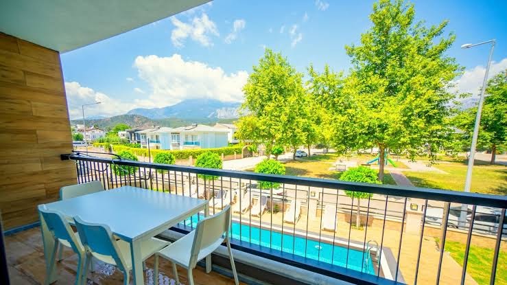Skats no Camyuva Beach Hotel balkona uz āra baseinu, zaļo dārzu un kalniem tālumā Kemeras reģionā