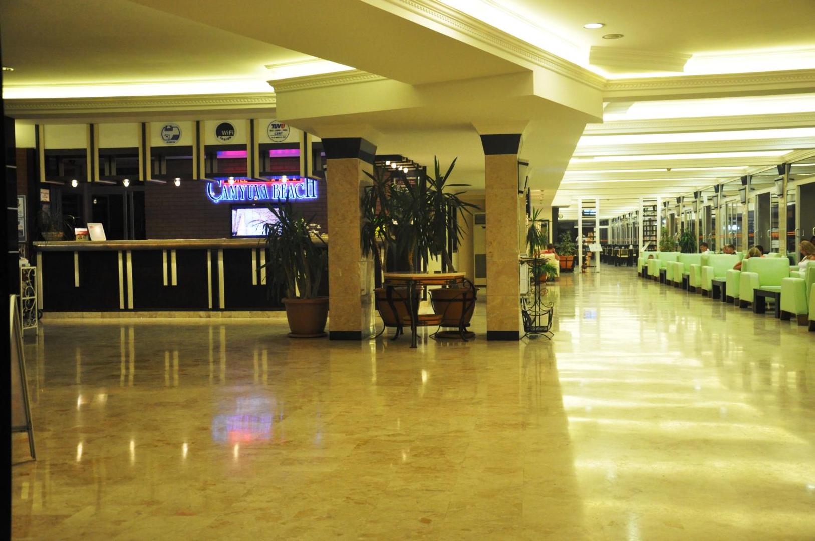 Camyuva Beach Hotel plašais un gaišais vestibils ar recepcijas leti, atpūtas zonu un spīdīgām marmora grīdām vakarā