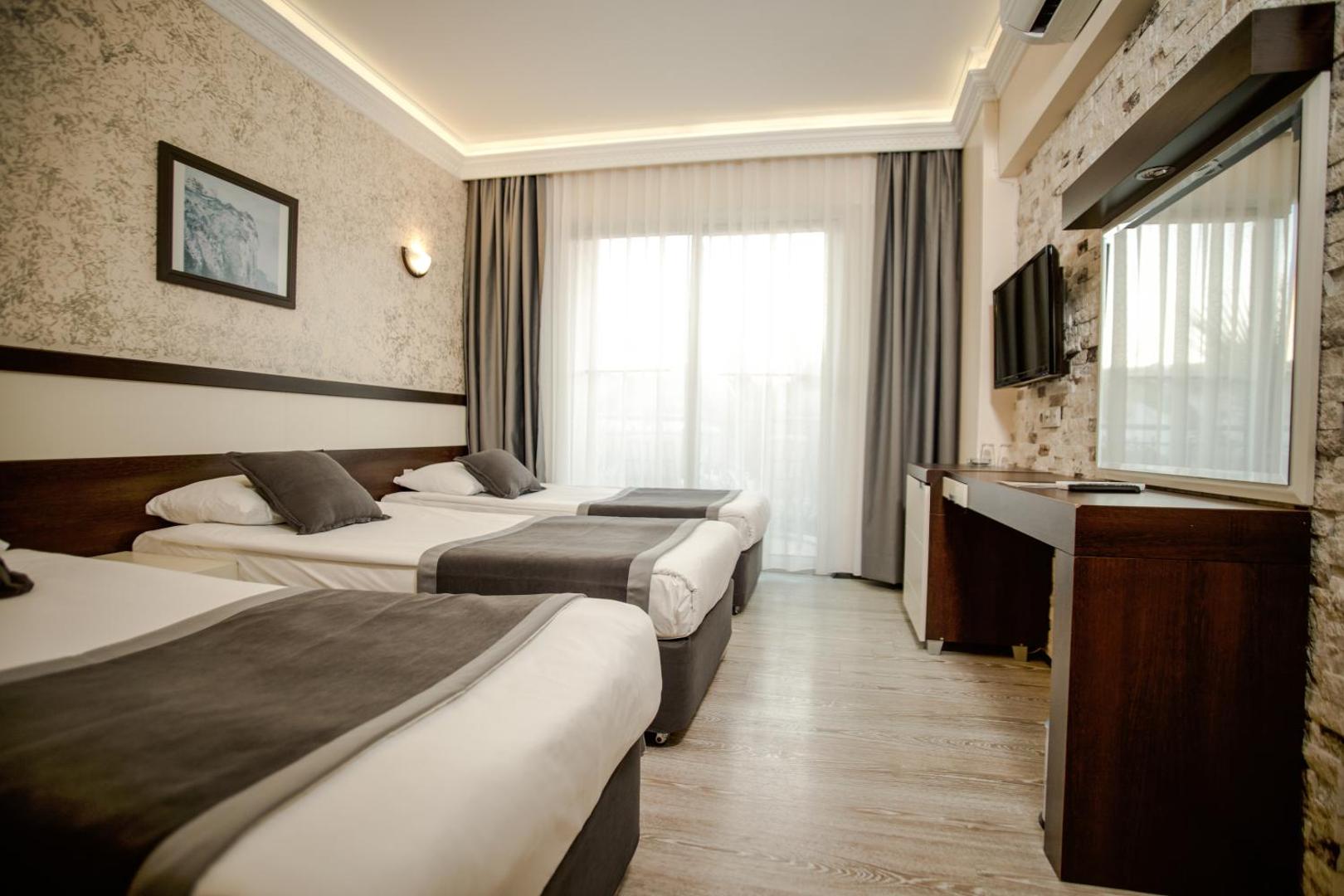 Viesnīcas Camyuva Beach Hotel numura interjers ar trim gultām, lielu spoguli un izeju uz balkonu Kemeras kūrortā