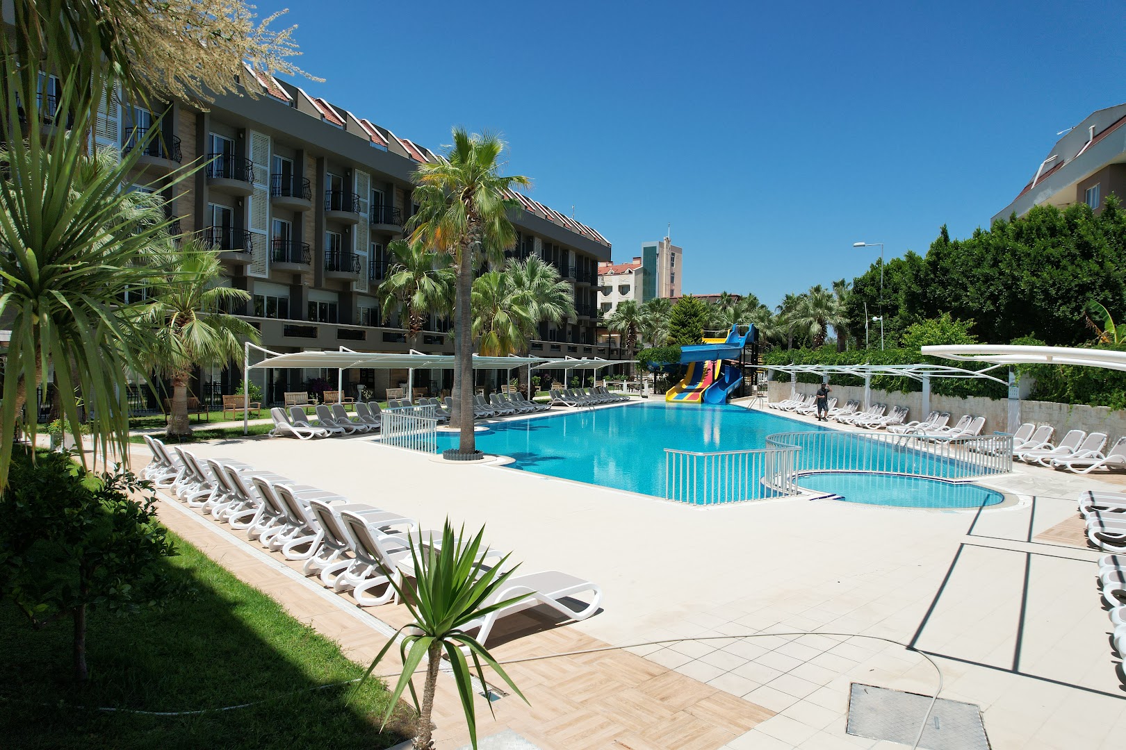 Camyuva Beach Hotel baseina teritorija ar bērnu baseinu, slidkalniņiem un viesnīcas fasādi saulainā dienā Turcijā