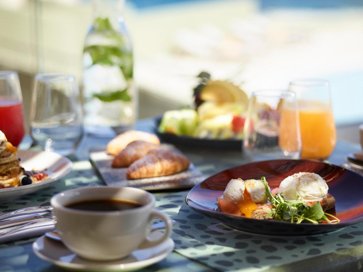 Brokastu galds Cayo Exclusive Resort and Spa ar olām Benedikta gaumē, kruasāniem, svaigiem augļiem un kafiju pie baseina