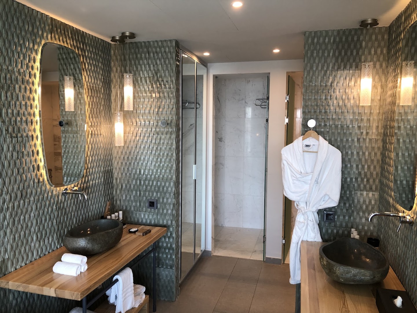 Cayo Exclusive Resort and Spa luksusa vannas numurs ar akmens izlietnēm, koka virsmām, modernu apgaismojumu un peldmēteli