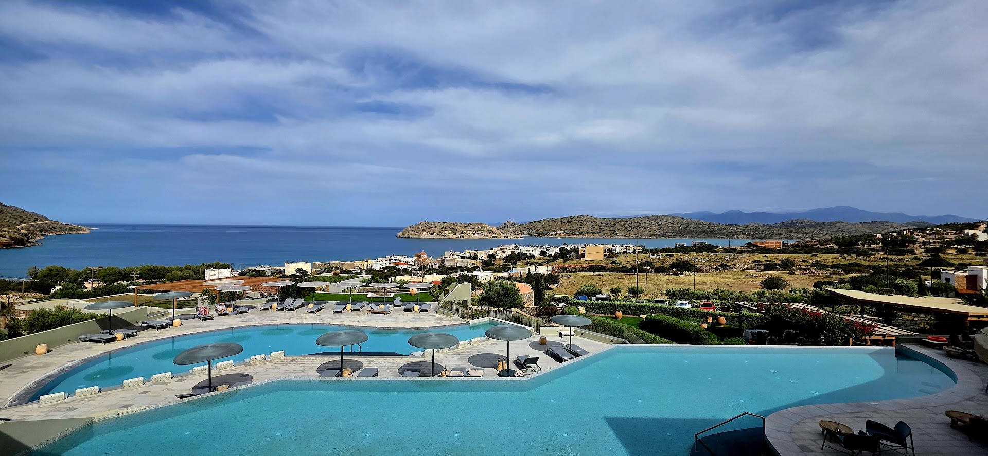 Cayo Exclusive Resort and Spa plašā baseinu teritorija ar saulessargiem un panorāmas skatu uz jūru un Spinalongas salu