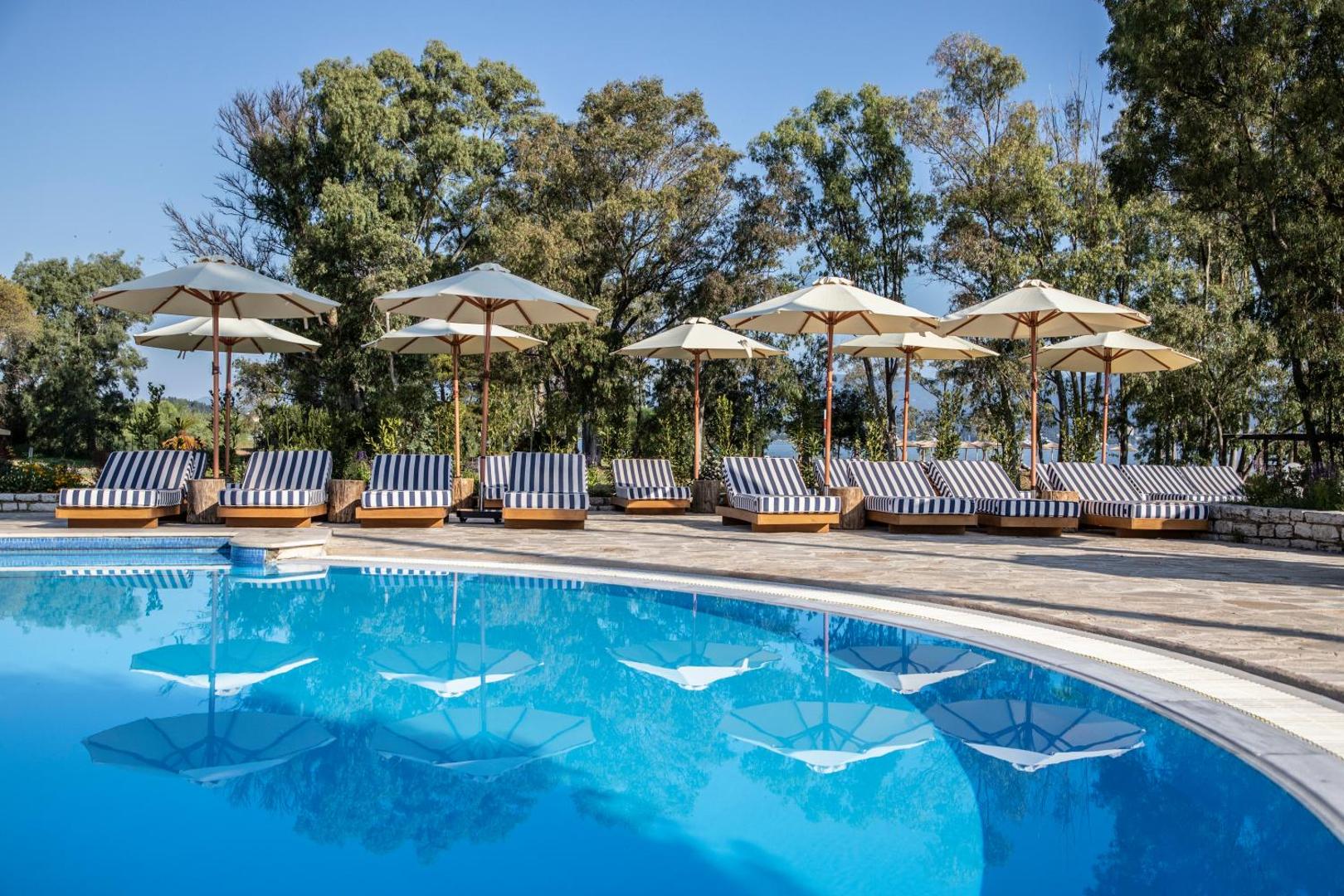 Kerkyra Blue Hotel & Spa āra baseins Korfu salā ar svītrainiem zviļņiem un saulessargiem koku ēnā pie ūdens malas