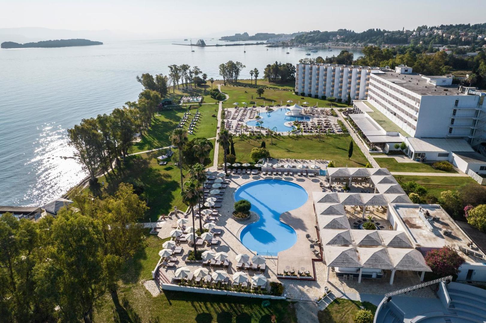 Kerkyra Blue Hotel & Spa āra baseinu zona ar sauļošanās krēsliem un saulessargiem, skats uz jūru un tuvējām salām Korfu piekrastē