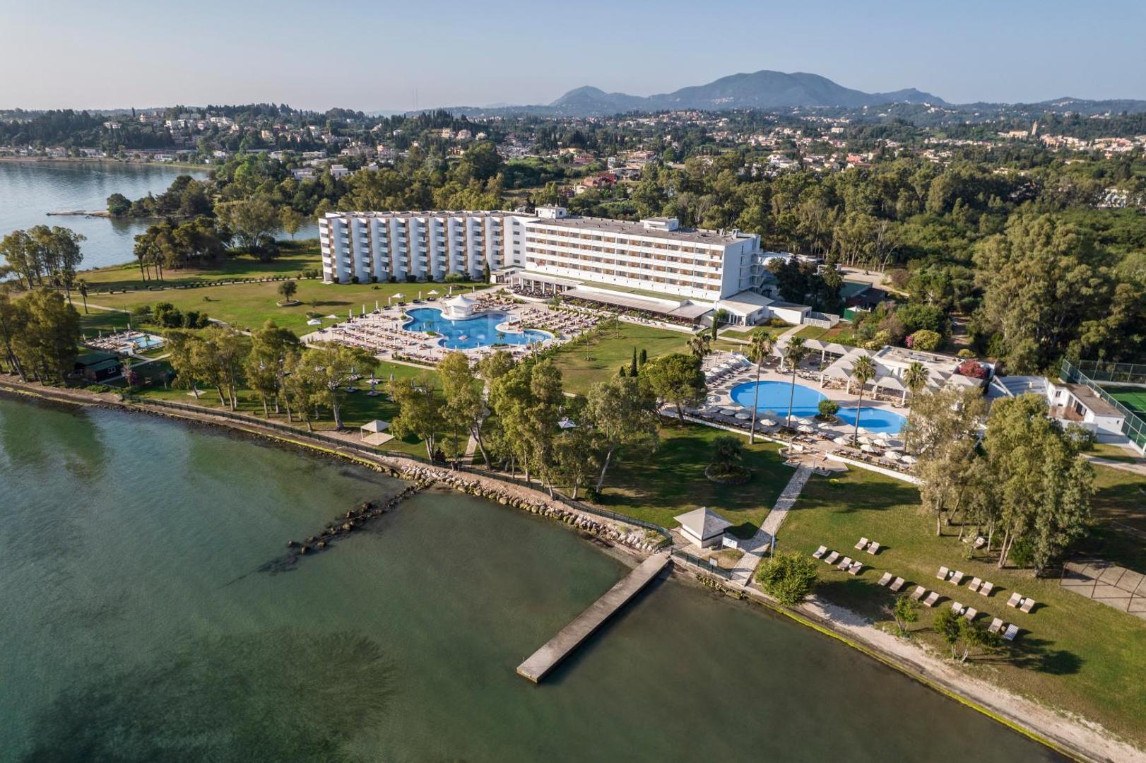 Kerkyra Blue Hotel & Spa panorāmas skats no putna lidojuma Korfu salā — viesnīcas ēka, baseini un zaļā teritorija pie Jonijas jūras