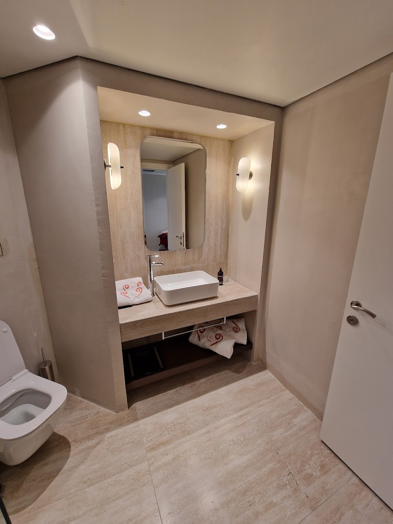 Kerkyra Blue Hotel & Spa numura vannasistaba ar modernu dizainu, akmens apdari, taisnstūra izlietni un lielu spoguli Korfu salā.