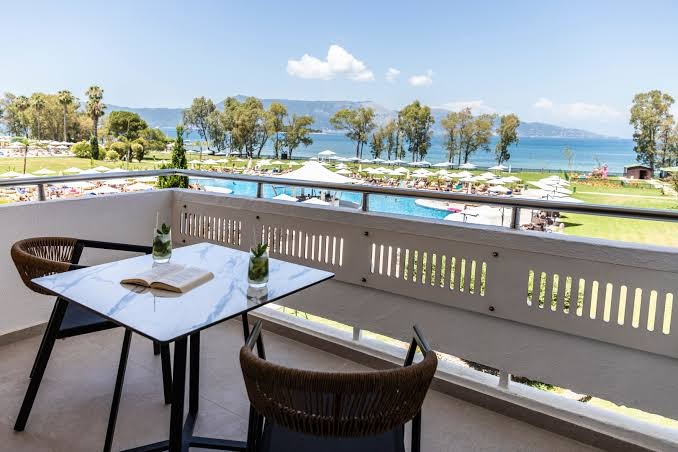 Skats no Kerkyra Blue Hotel & Spa numura balkona uz baseinu zonu un jūru, galds ar atspirdzinošiem dzērieniem