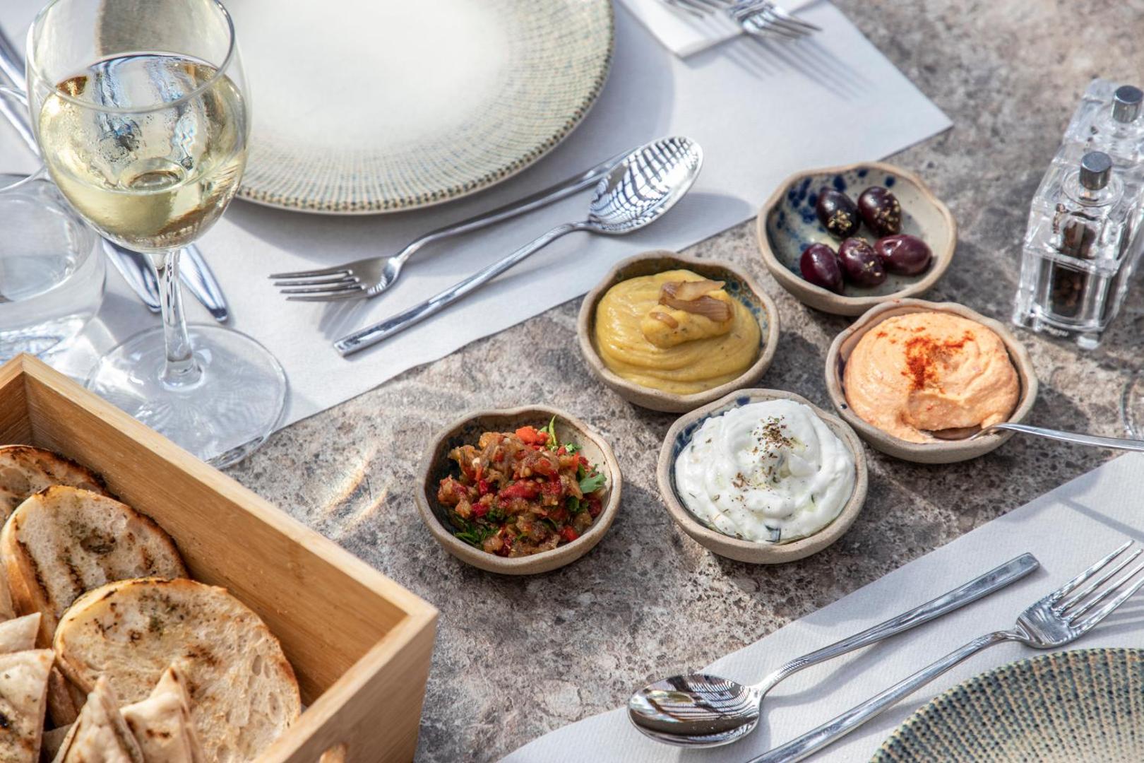 Vidusjūras reģiona uzkodas un meze Kerkyra Blue Hotel & Spa restorānā — humuss, olīvas un svaiga maize uz terases galda