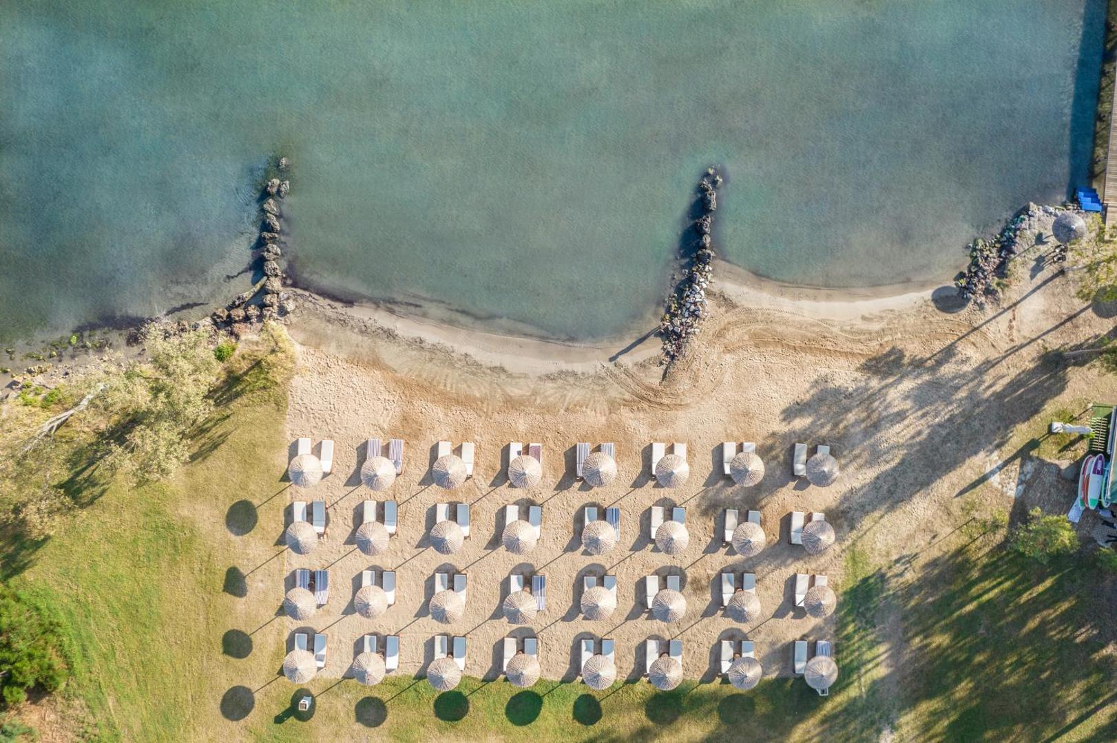 Aerofoto skats uz Kerkyra Blue Hotel & Spa privāto pludmali Korfu — saulessargi un sauļošanās krēsli pie dzidra ūdens