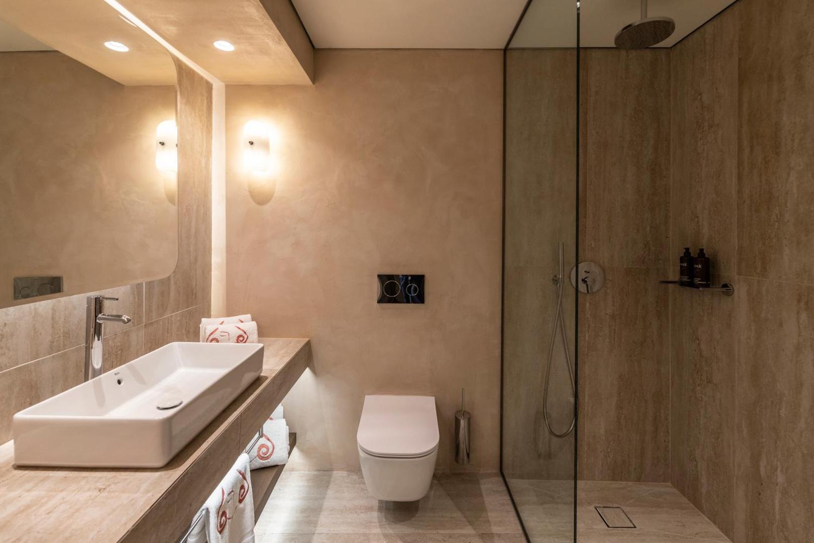 Kerkyra Blue Hotel & Spa moderns vannas numurs ar stikla dušas kabīni, akmens apdari un siltu apgaismojumu