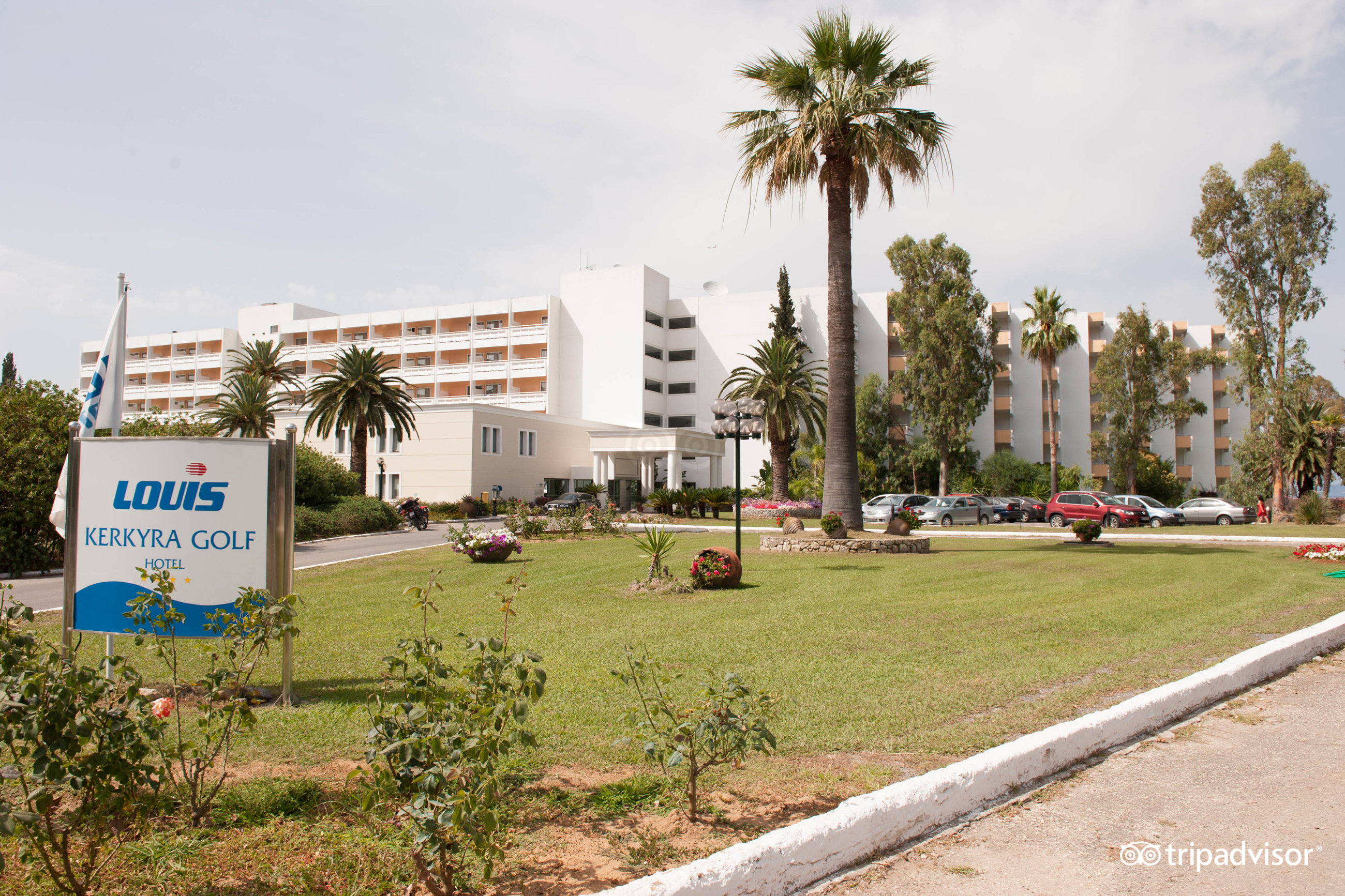 Kerkyra Blue Hotel & Spa galvenā ieeja un fasāde ar palmām un koptu mauriņu, redzama viesnīcas informatīvā zīme