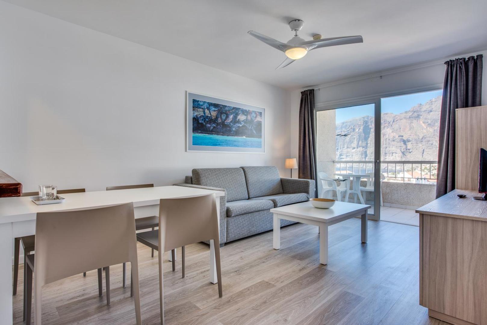 Vigilia Park Apartamentos apartamentu viesistaba ar skatu caur balkona durvīm uz Los Gigantes klintīm Tenerifē