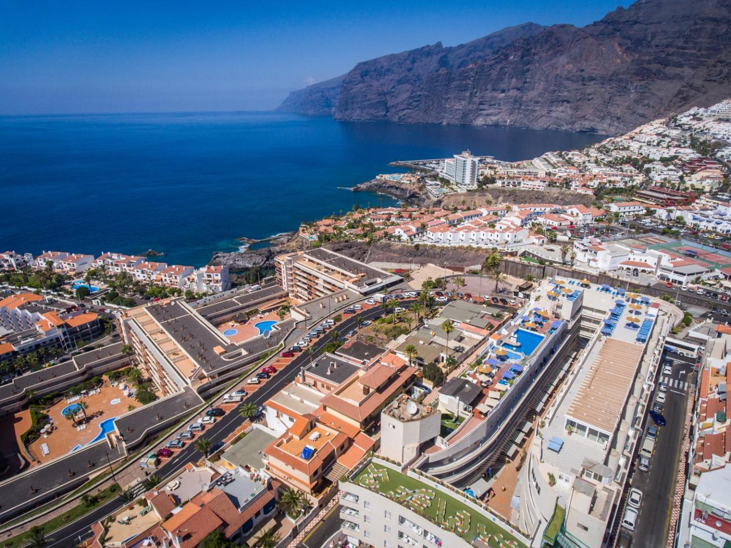 Vigilia Park Apartamentos skats no putna lidojuma Puertodesantiago pilsētā Tenerifē ar Los Gigantes klintīm un zilo okeānu fonā