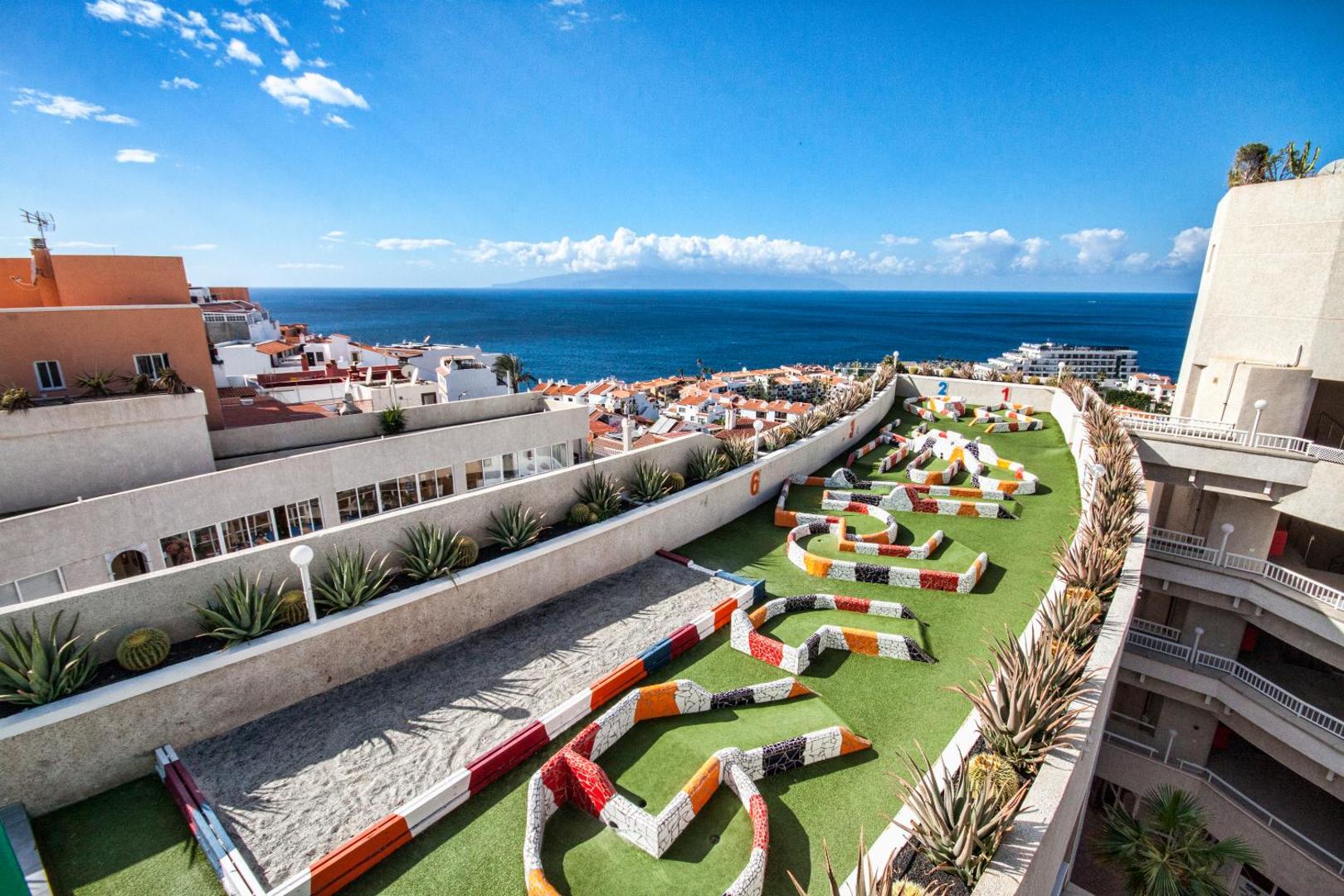 Vigilia Park Apartamentos minigolfa laukums uz jumta terases ar skatu uz okeānu un pilsētu Tenerifē — krāsainas joslas un mākslīgais zāliens