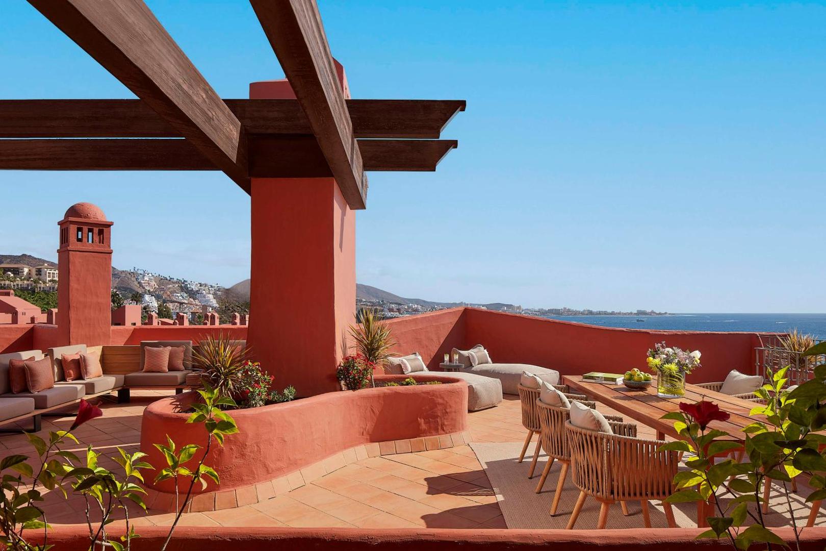 Tivoli La Caleta Tenerife Resort plaša jumta terase ar atpūtas mēbelēm, pusdienu galdu un skatu uz okeānu Tenerifes piekrastē.