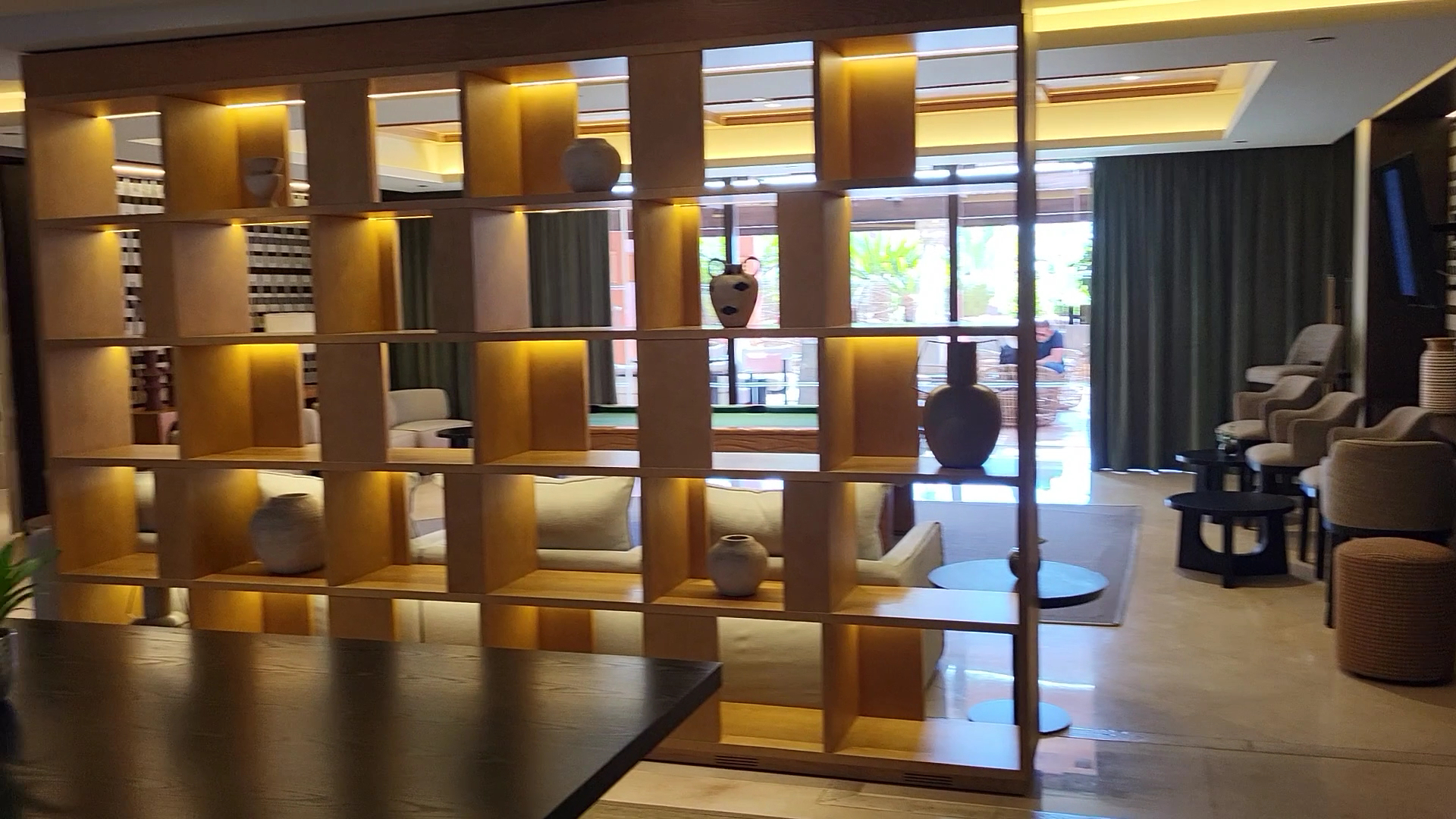 Tivoli La Caleta Tenerife Resort lobby atpūtas zona ar dekoratīvu koka plauktu, mīkstajiem krēsliem un siltu apgaismojumu Tenerifes piekrastē.