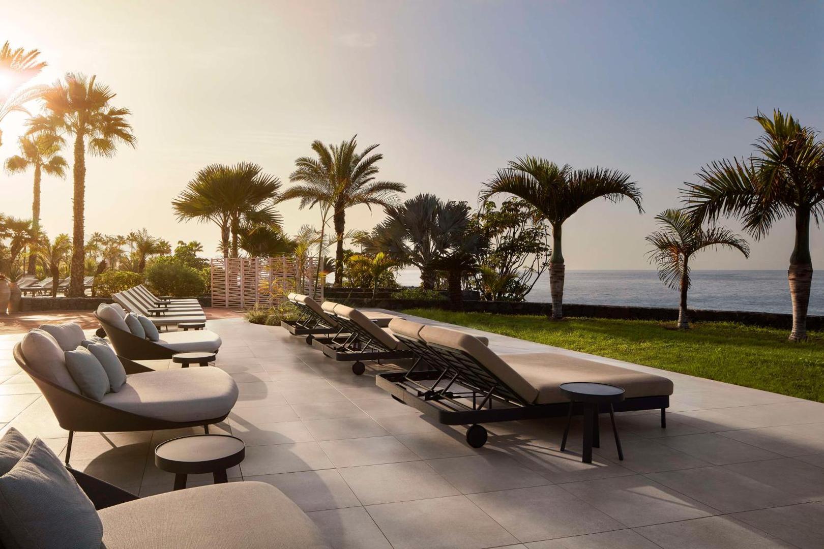 Tivoli La Caleta Tenerife Resort atpūtas zona ar mīkstiem zviļņiem un skatu uz okeānu saulrietā, Tenerifes piekrastē.