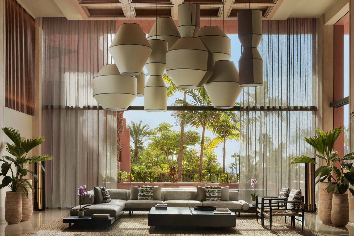 Tivoli La Caleta Tenerife Resort gaišā lobby atpūtas zona ar augstiem griestiem, dizaina lampām un skatu uz palmu dārzu