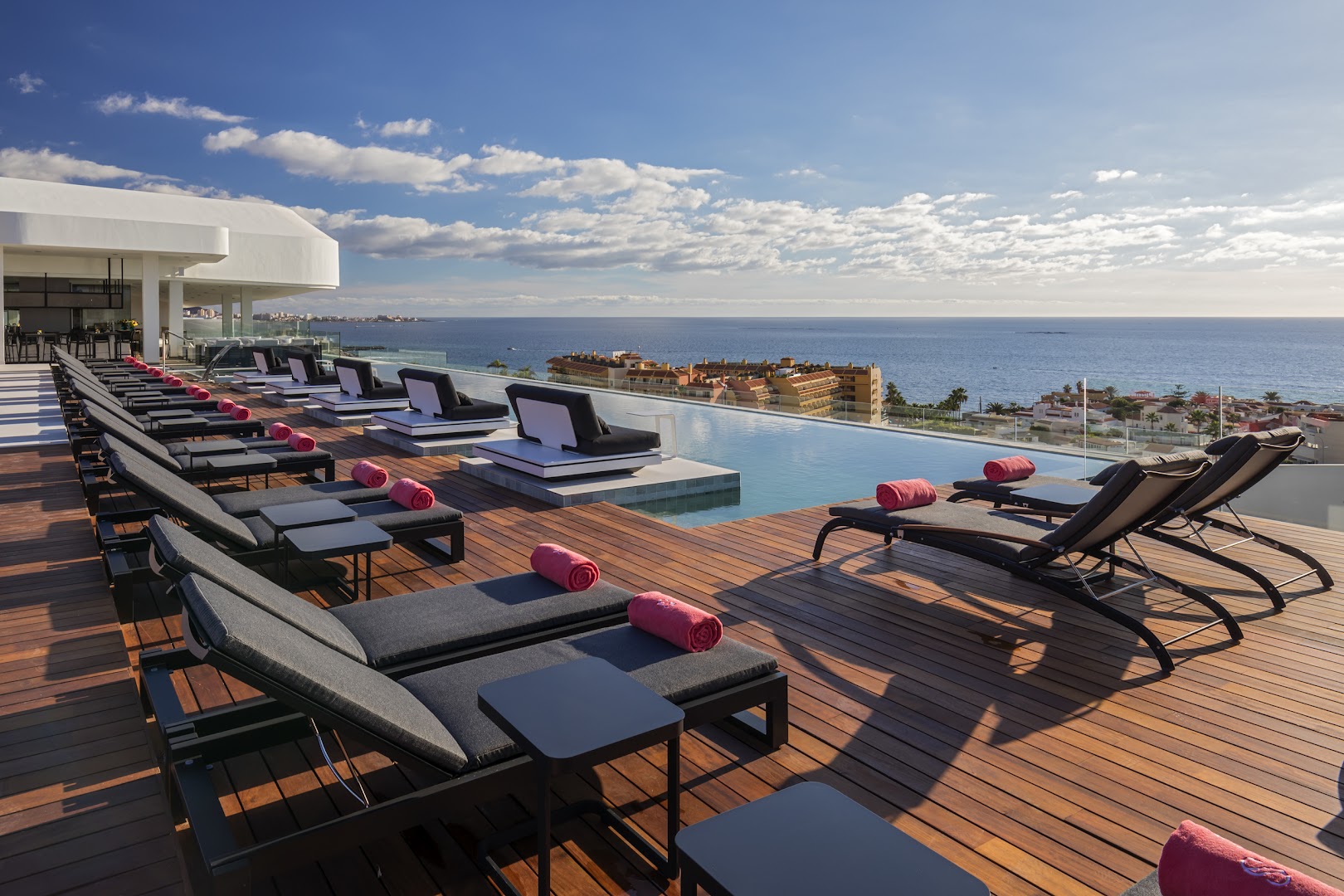 Royal Hideaway Corales Suites jumta terase ar koka klāju, sauļošanās krēsliem un panorāmas skatu uz okeānu un pilsētu
