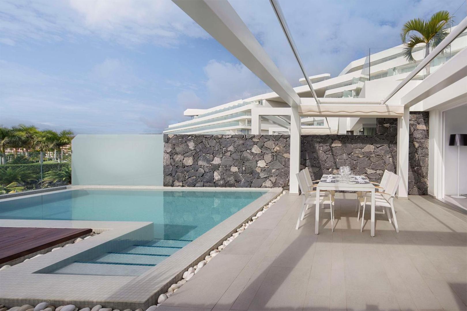Royal Hideaway Corales Suites privātais numura baseins un terase ar pusdienu galdu, akmens sienu un skatu uz viesnīcas ēku