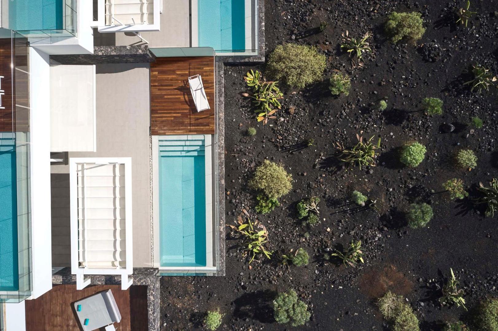 Aerofoto uzņēmums Royal Hideaway Corales Suites numuriem ar baseiniem blakus vulkāniskas izcelsmes dārzam ar eksotiskiem augiem.