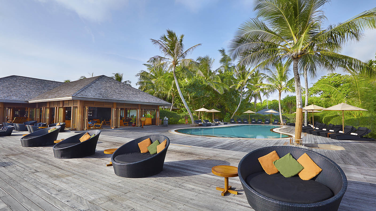 Kuredu Island Resort & Spa atpūtas zona ar apaļiem dīvāniem uz koka klāja pie baseina un tropu dārza
