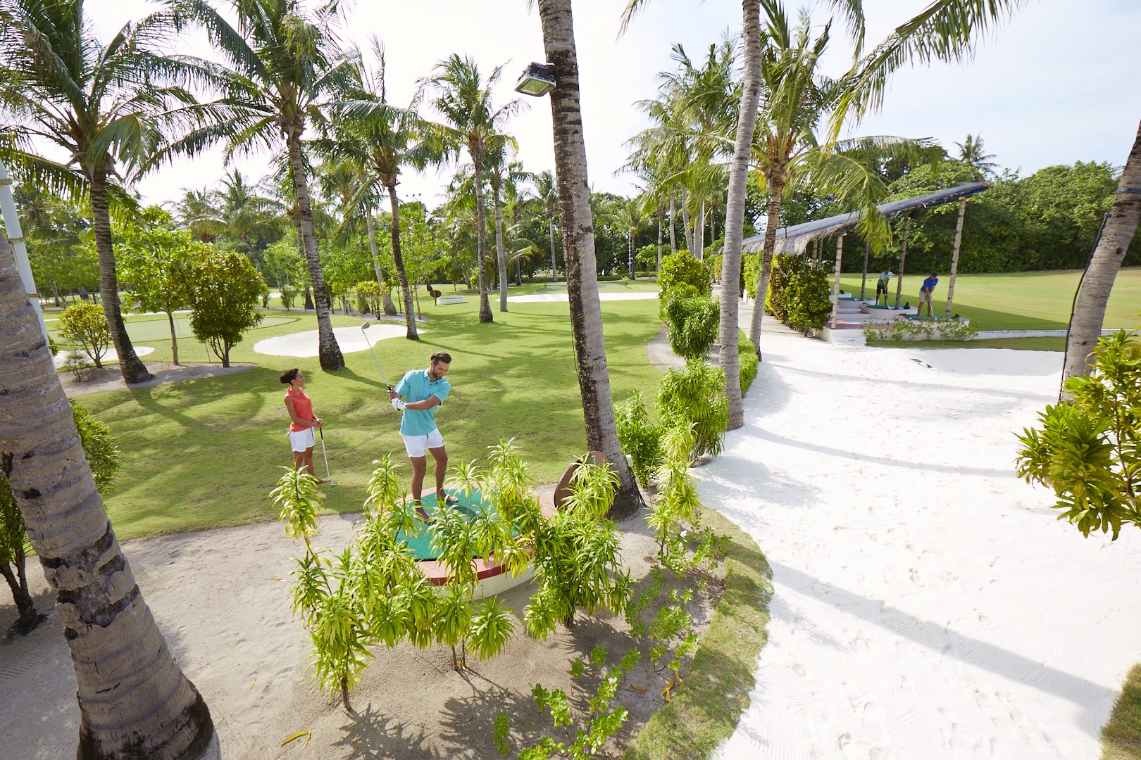 Kuredu Island Resort & Spa golfa laukums ar palmām un spēlētājiem saulainā dienā Maldīvu salu piekrastē